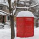 Brick red porta potty rental toilet covered with snow - renting a porta potty in the winter